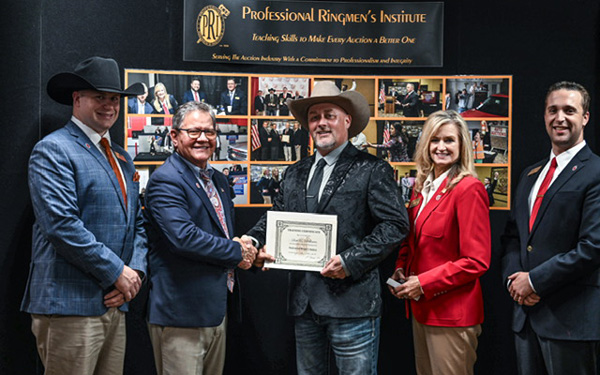 Five professionals on a stage present a certificate during an awards ceremony, with a man in a cowboy hat receiving it from a colleague while others look on.