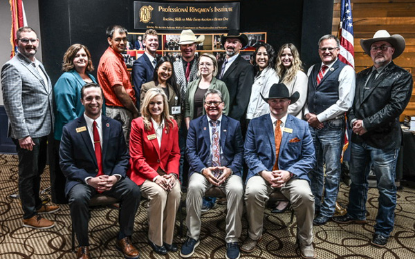 Group of professionals posing for a group photo at a conference, with a banner and the US flag visible in the background.